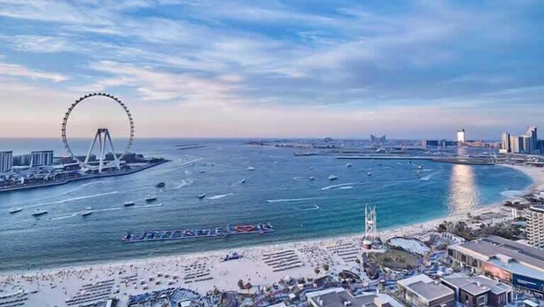 A coastal cityscape with a prominent Ferris wheel, a marina with boats, and a beach area with buildings and a hotel. - Premium 3BR plus maid room -Beachfront -Monthly Stay (Dubai)