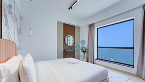 A hotel room with a large bed, a view of the sea, a wooden headboard, and a modern light fixture. - Premium 3BR plus maid room -Beachfront -Monthly Stay (Dubai)