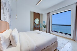 Ein Hotelzimmer mit einem großen Bett, Meerblick, einem hölzernen Kopfteil und einer modernen Lampe.