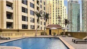 A swimming pool surrounded by a building with balconies and a small structure with umbrellas. - Premium 3BR plus maid room -Beachfront -Monthly Stay (Dubai)