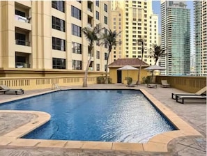 A swimming pool surrounded by a building with balconies and a small structure with umbrellas. - Premium 3BR plus maid room -Beachfront -Monthly Stay (Dubai)