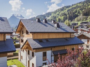 Ein Wohngebäude mit geneigtem Dach, mehreren Schornsteinen und Blick auf einen Berg im Hintergrund.