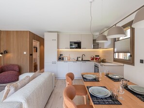 Eine moderne Küche mit weißen Schränken, einem eingebauten Backofen und einem Essbereich mit einem Holztisch, gedeckt für vier Personen.