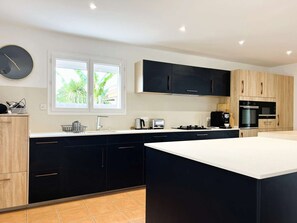 A modern kitchen with dark cabinets, a large island, a window with a view of greenery, and built-in appliances.
