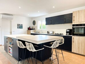 A modern kitchen with a central island, bar stools, a built-in oven, and a coffee machine.