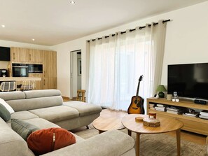 A modern living room with a sectional sofa, a TV, a guitar, and a small dining area.