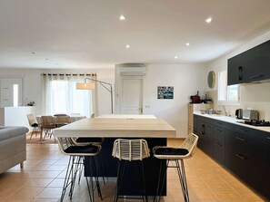 A modern kitchen with a central island, bar stools, and a dining area with a sofa and chairs.