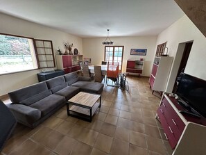 Ein Wohnzimmer mit einer Couch, einem Couchtisch, einem Esstisch mit Stühlen, einem Fernseher und Küchenschränken.