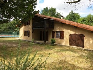 Ein zweistöckiges Gebäude mit rotem Ziegeldach, einem Balkon und einem eingezäunten Tennisplatz im Hintergrund.