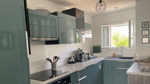 A modern kitchen with teal cabinets, a built-in oven, a coffee maker, and a window providing natural light. - Modern villa with pool and parking - La Grande Motte (La Grande-Motte)