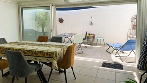 A dining area with a table and chairs, a sliding glass door leading to an outdoor patio with a blue chair and a potted plant. - Modern villa with pool and parking - La Grande Motte (La Grande-Motte)
