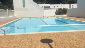 A rectangular swimming pool with a tiled deck, a green door, and a white building in the background. - Modern villa with pool and parking - La Grande Motte (La Grande-Motte)