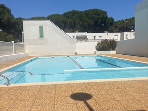 Ein rechteckiger Swimmingpool mit Fliesen umrandet, eine grüne Tür und ein weißes Gebäude im Hintergrund.