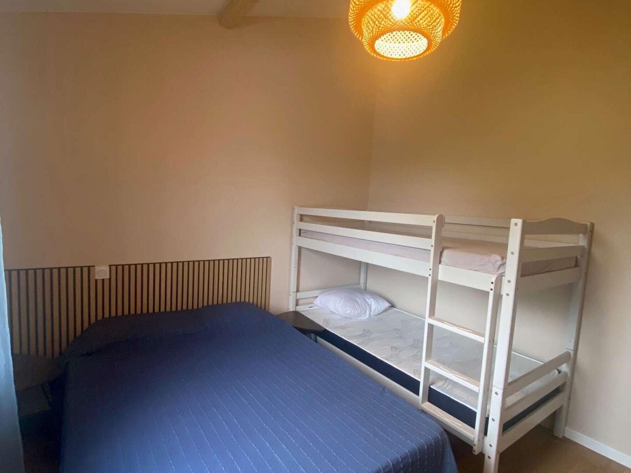 Un lit superposé avec un matelas bleu et un oreiller blanc, un plafond en pente et un luminaire suspendu.