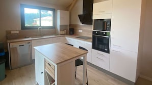 Ett kompakt kök med inbyggd diskmaskin, mikrovågsugn och ugn. Ett fönster släpper in naturligt ljus, och köket har en enkel och funktionell design.