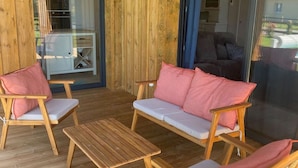 Ett trädäck med en soffa och stolar, ett litet bord och en glasdörr som leder in till ett inomhusutrymme.