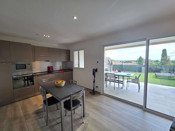 A modern kitchen with a dining area, sliding glass doors to an outdoor patio, and a view of a green lawn. - Apartment with air conditioning, terrace - 3 guests (Lumio)
