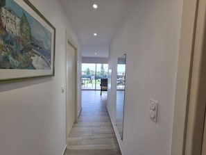 A hallway with a painting on the left, a door at the end, and a view of an outdoor patio area. - Apartment with air conditioning, terrace - 3 guests (Lumio)