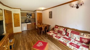 A compact living space with a kitchenette, a wooden dining table, a sofa, and a small wooden cabinet. - Comfortable and bright apartment - 4 guests (Valloire)