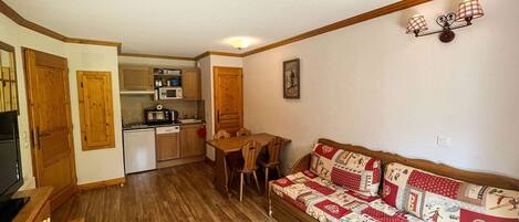 A compact living space with a kitchenette, a wooden dining table, a sofa, and a small wooden cabinet.
