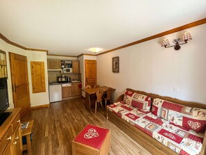 A compact living space with a kitchenette, a wooden dining table, a sofa, and a small wooden cabinet. - Comfortable and bright apartment - 4 guests (Valloire)