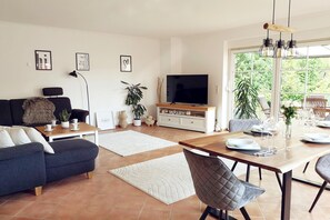 Ein modernes Wohnzimmer mit Sofa, Fernseher, Esstisch und Stühlen.