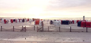 Ein Strand mit Reihen von Strandkörben, einem Zaun und einem Leuchtturm im Hintergrund.