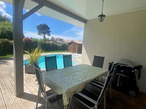 Eine überdachte Terrasse mit Pool, Tisch, Stühlen und Grill.