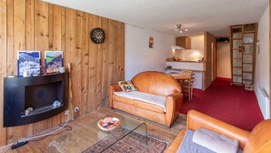 Un salon avec une cheminée, des murs en bois, un canapé, un coin repas et une moquette rouge.