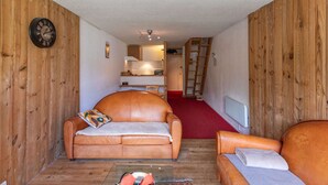 Un salon chaleureux avec deux canapés en cuir, une horloge murale en bois et un tapis rouge qui mène à un espace cuisine.