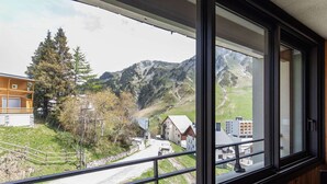 Une vue depuis une fenêtre donnant sur un paysage rural, avec des montagnes, une route et des bâtiments.