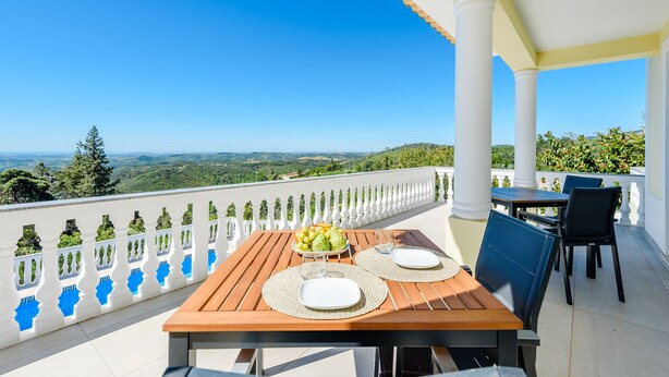 A balcony with a table set for two, a fruit bowl, and a view of the landscape. - Villa Montinho Vista (Monchique)