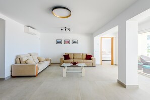 A spacious living room with a beige sofa, a glass coffee table, and a modern ceiling light fixture. - Villa Montinho Vista (Monchique)