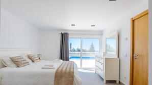 A bedroom with a bed, a dresser, a door, and a balcony with a view. - Villa Montinho Vista (Monchique)