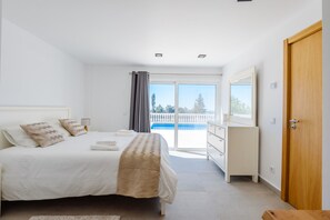 A bedroom with a bed, a dresser, a door, and a balcony with a view. - Villa Montinho Vista (Monchique)