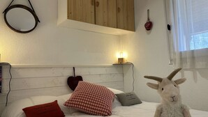 Une chambre à coucher avec une tête de lit en bois, un lit avec une literie blanche, un oreiller rouge, un oreiller gris et un animal en peluche.