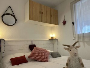 Een slaapkamer met een houten hoofdbord, een bed met witte beddengoed, een rood kussen, een grijs kussen en een pluche speeltje.