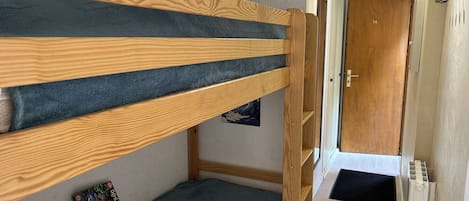 A bunk bed with a blue mattress, a wooden headboard, and a small shelf with books and a picture frame.