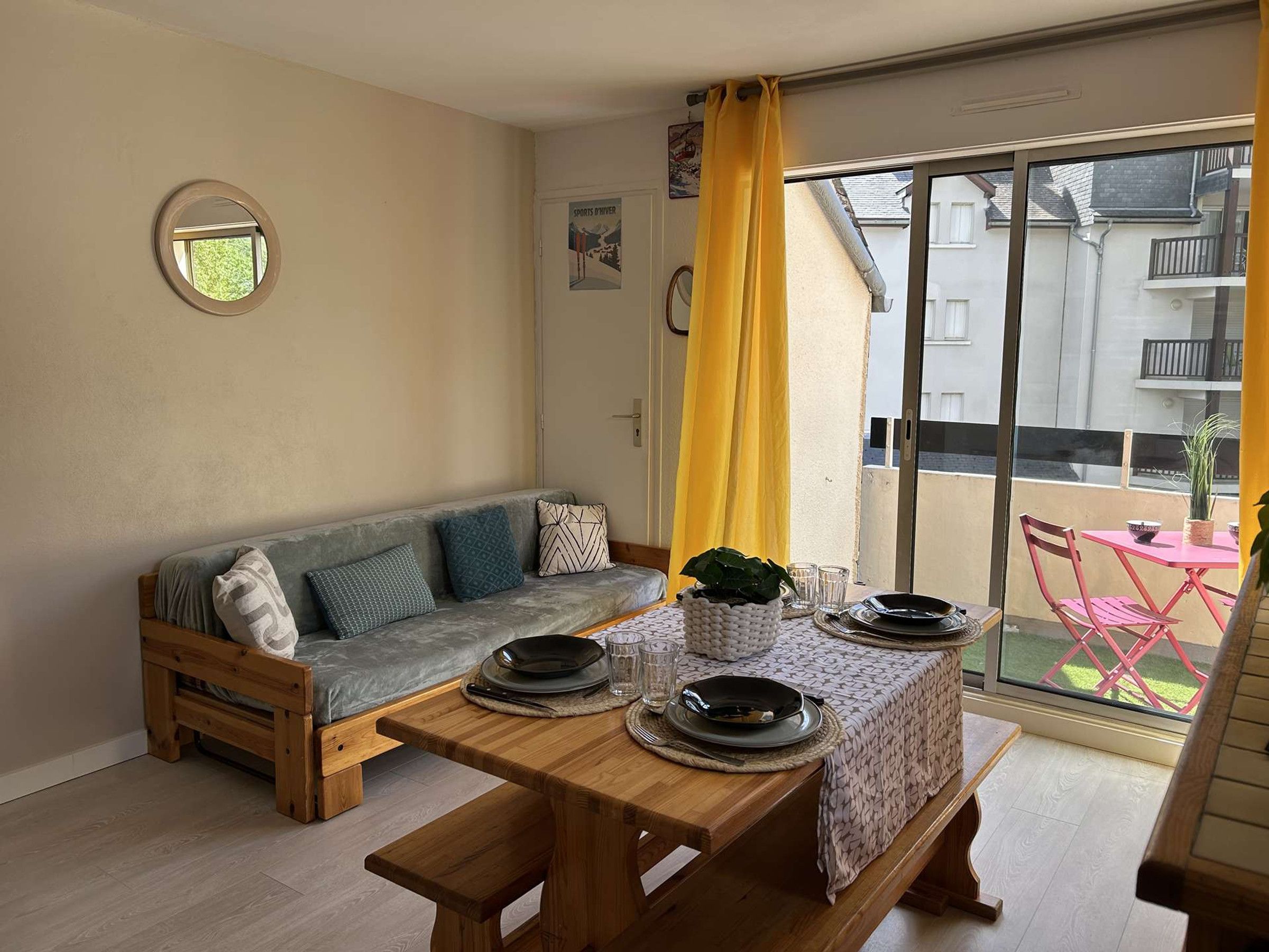 A cozy living area with a sofa, a wooden table set for dining, and a large window with a view of the outside.