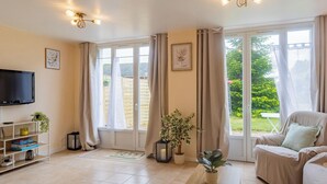 A spacious living room with a television, a sofa, a coffee table, and large windows with curtains.