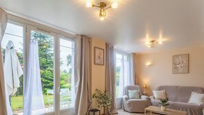 A room with large windows, a sofa, a chair, a small table, and wall-mounted lighting.