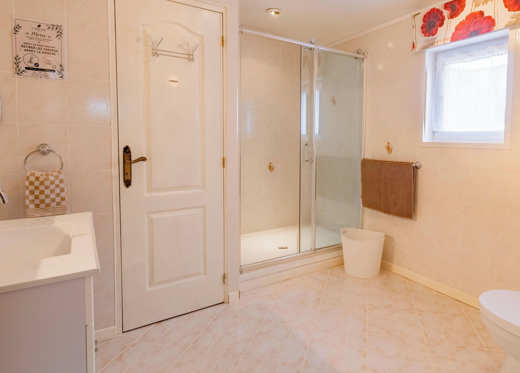 Et badeværelse med brusebad, toilet, håndvask og et håndklædetørrestativ samt et vindue.
