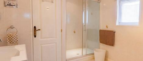 Et badeværelse med brusebad, toilet, håndvask og et håndklædetørrestativ samt et vindue.