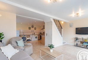 A living room with a sofa, a coffee table, a TV, and a staircase leading to a kitchen. - Charming and bright country cottage - 4 guests (Saint-Philbert-du-Peuple)
