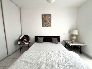 A bedroom with a bed, a chair, a bedside table with a lamp, and a wall-mounted painting. - House with parking, pets allowed - 4 guests (Léon)