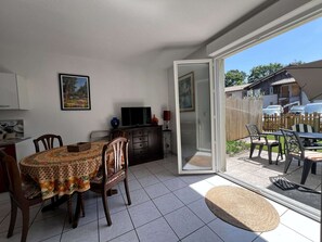 A dining area with a table and chairs, a television on a cabinet, and a sliding glass door leading to an outdoor patio.