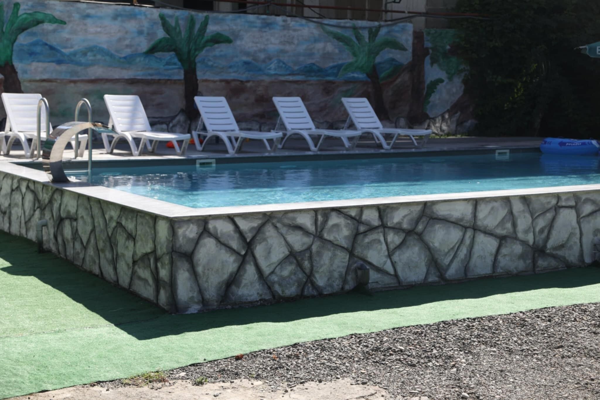 A swimming pool with white lounge chairs, a stone wall, and a mural of palm trees and mountains.