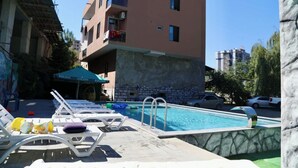 Una piscina con sillas de descanso, un muro de piedra y un edificio de varios pisos al fondo.