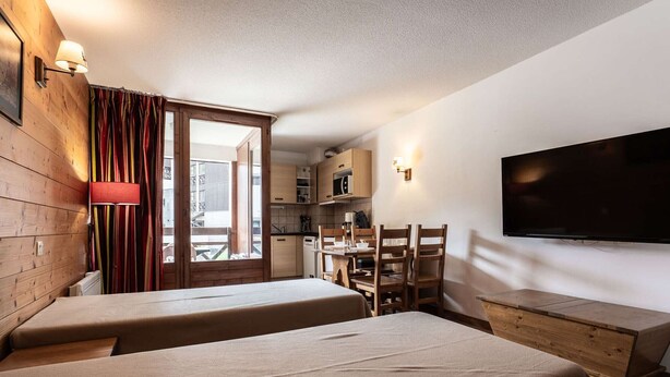 Una habitación con dos camas, televisión, kitchenette y balcón con cortinas.