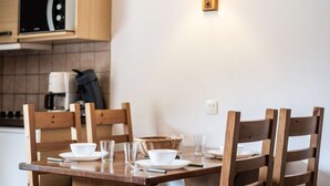 Una mesa de comedor dispuesta con platos blancos, vasos y una cesta, en una habitación con sillas de madera y un microondas al fondo.